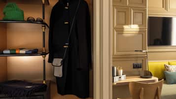Habitación de hotel con cama, escritorio, silla, televisor, estante con ropa y perchero.