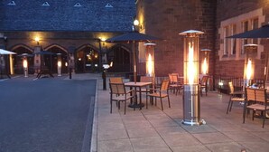 An outdoor seating area with tables and chairs, surrounded by brick walls and illuminated by tall, cylindrical lanterns. - The Stirling Highland Hotel (Stirling)