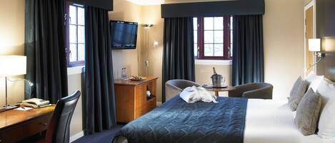 Habitación de hotel con cama, escritorio, silla, televisor y ventana con cortinas.