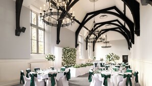 A banquet hall with multiple round tables, white tablecloths, and green chair sashes. - The Stirling Highland Hotel (Stirling)