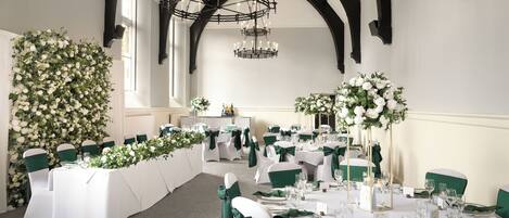 A banquet hall with white tables, green chair sashes, and floral arrangements.
