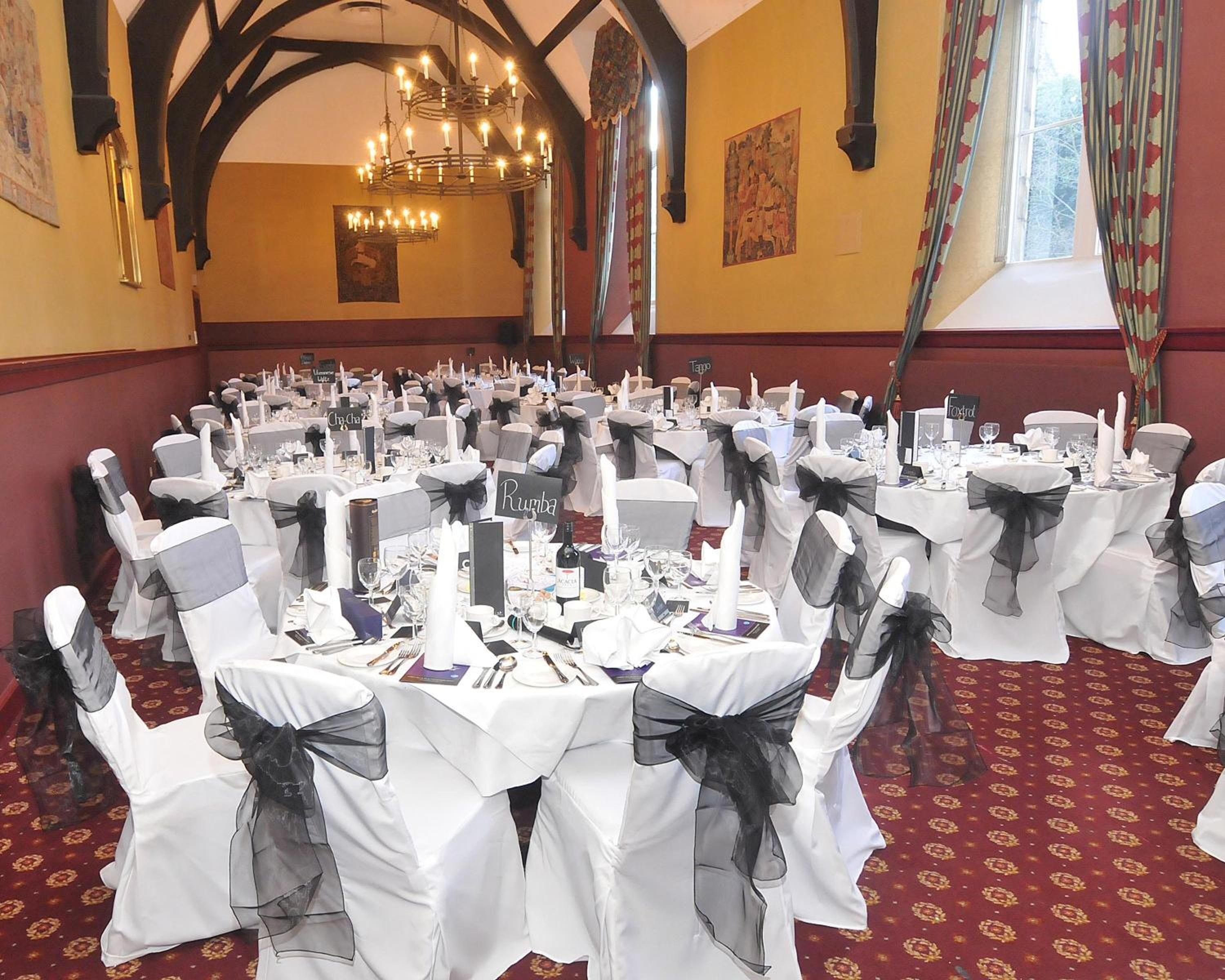A banquet hall with round tables, white tablecloths, and chairs with black sashes.