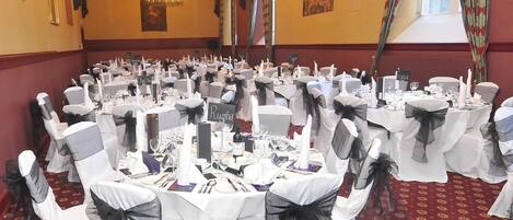 A banquet hall with round tables, white tablecloths, and chairs with black sashes.