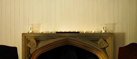 Mesa de comedor dispuesta para cuatro personas, con velas, candelabro y chimenea.