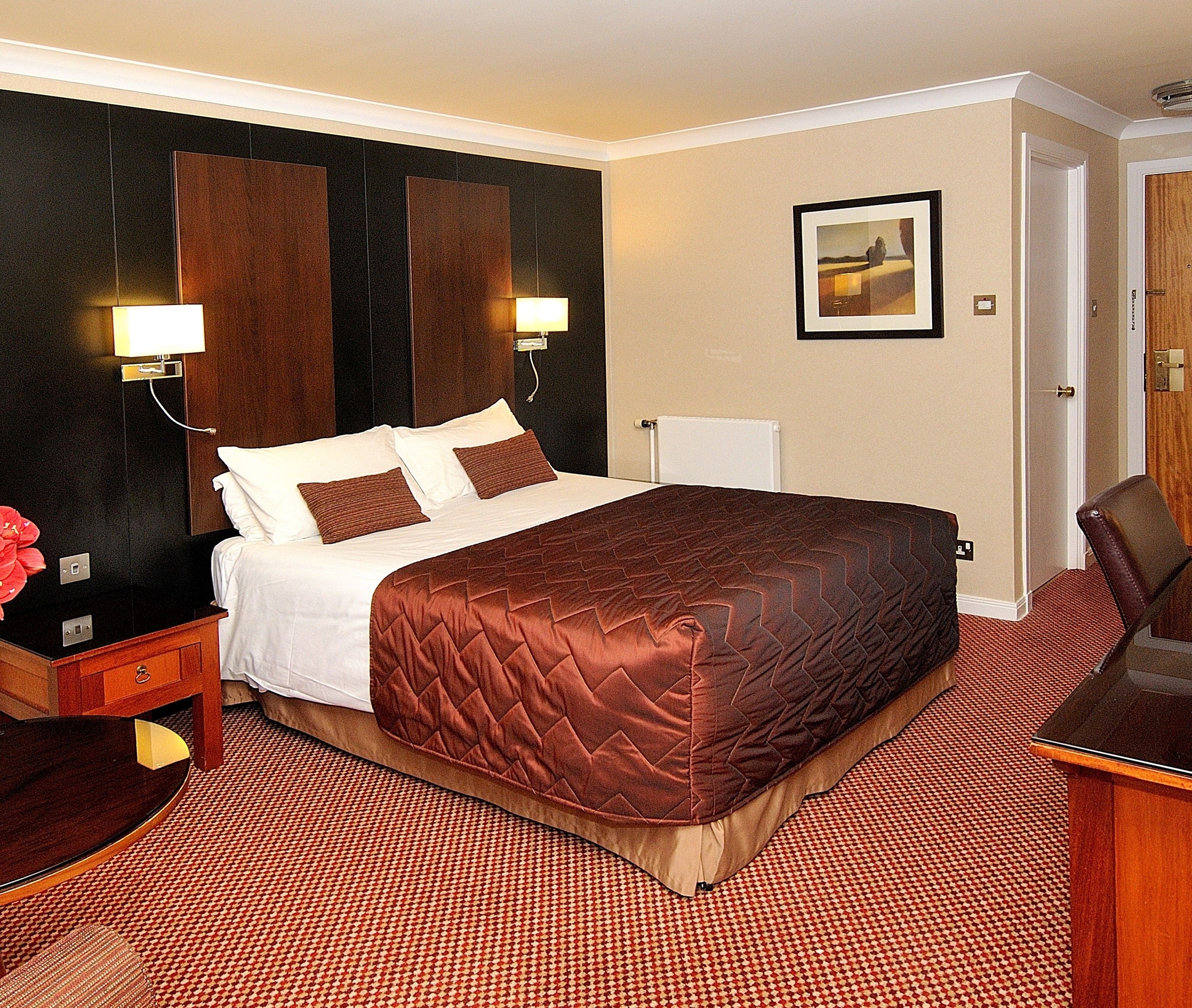 A hotel room with a large bed, two bedside tables, a nightstand, a desk, and a chair.