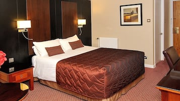 A hotel room with a large bed, two bedside tables, a nightstand, a desk, and a chair.