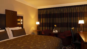 Ein Hotelzimmer mit einem großen Bett, zwei Sesseln, einem kleinen Tisch und einer Lampe.