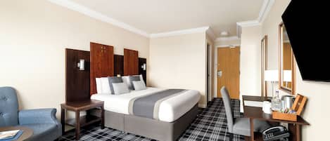 A hotel room with a bed, a desk with a chair, a small table, and a TV.