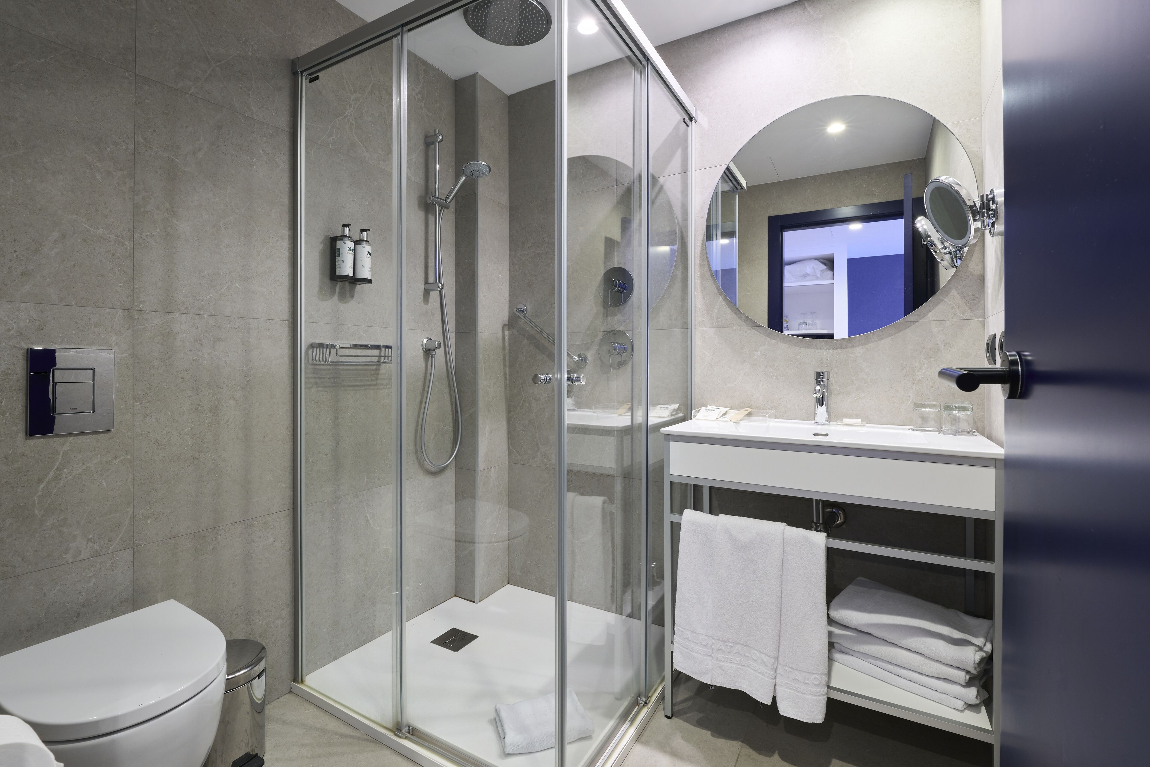 Un baño moderno con ducha envuelta en vidrio, un lavamanos blanco y un espejo sobre el lavamanos.