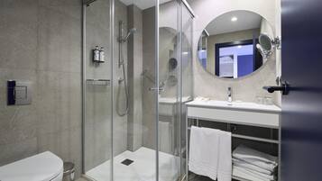 Un baño moderno con ducha envuelta en vidrio, un lavamanos blanco y un espejo sobre el lavamanos.