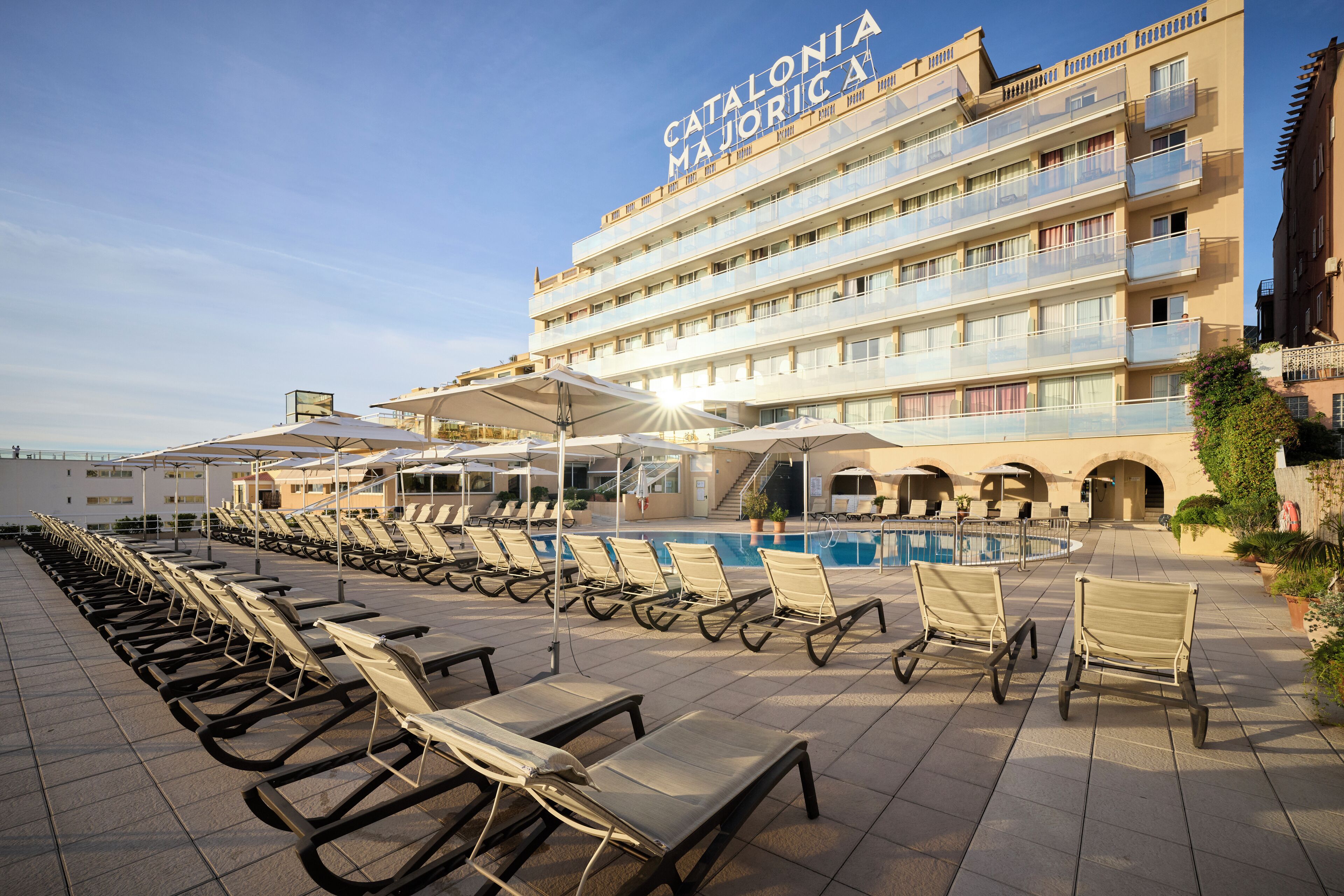 A hotel with a pool area, sun loungers, and a clear sky.