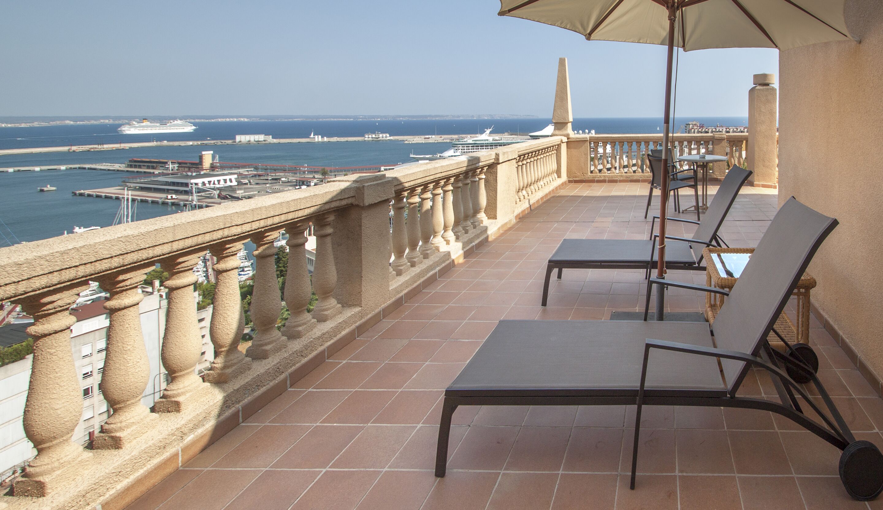 A balcony with a view of the sea, featuring a table and chairs, and a decorative balustrade.
