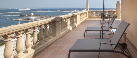 A balcony with a view of the sea, featuring a table and chairs, and a decorative balustrade.