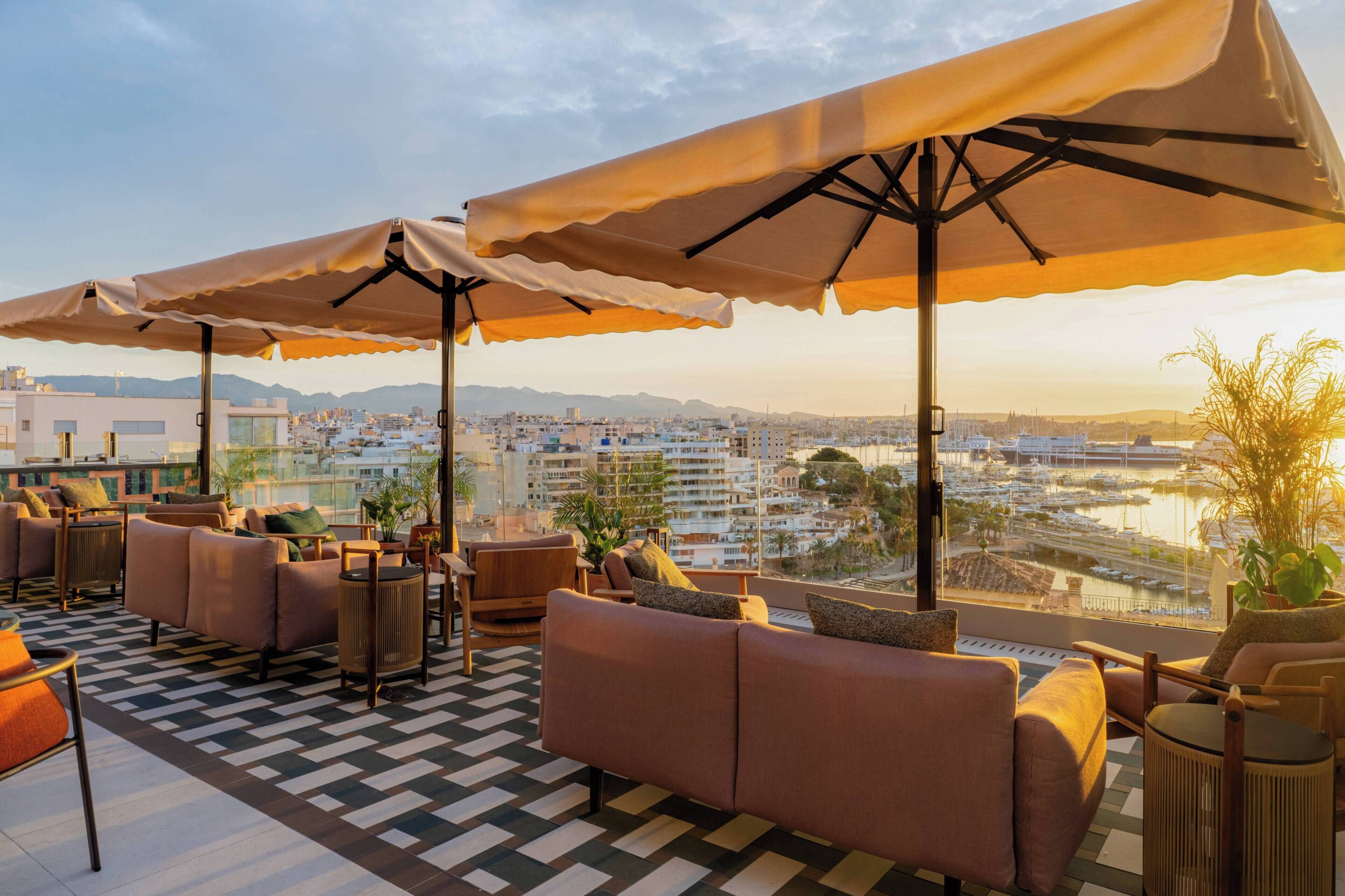 Eine Dachterrasse mit Sitzgelegenheiten im Freien, Sonnenschirmen und Blick auf einen Yachthafen sowie die Stadtlandschaft.