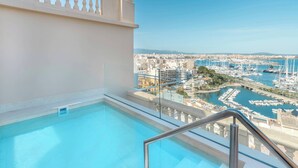 Una piscina en la azotea con barandilla de vidrio, con vistas a un puerto deportivo con barcos y edificios.