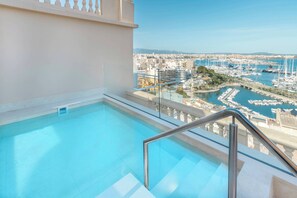 Una piscina en la azotea con barandilla de vidrio, con vistas a un puerto deportivo con barcos y edificios.