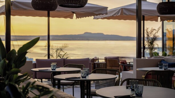 Un área de estar al aire libre con mesas, sillas, sombrillas y vista al mar.