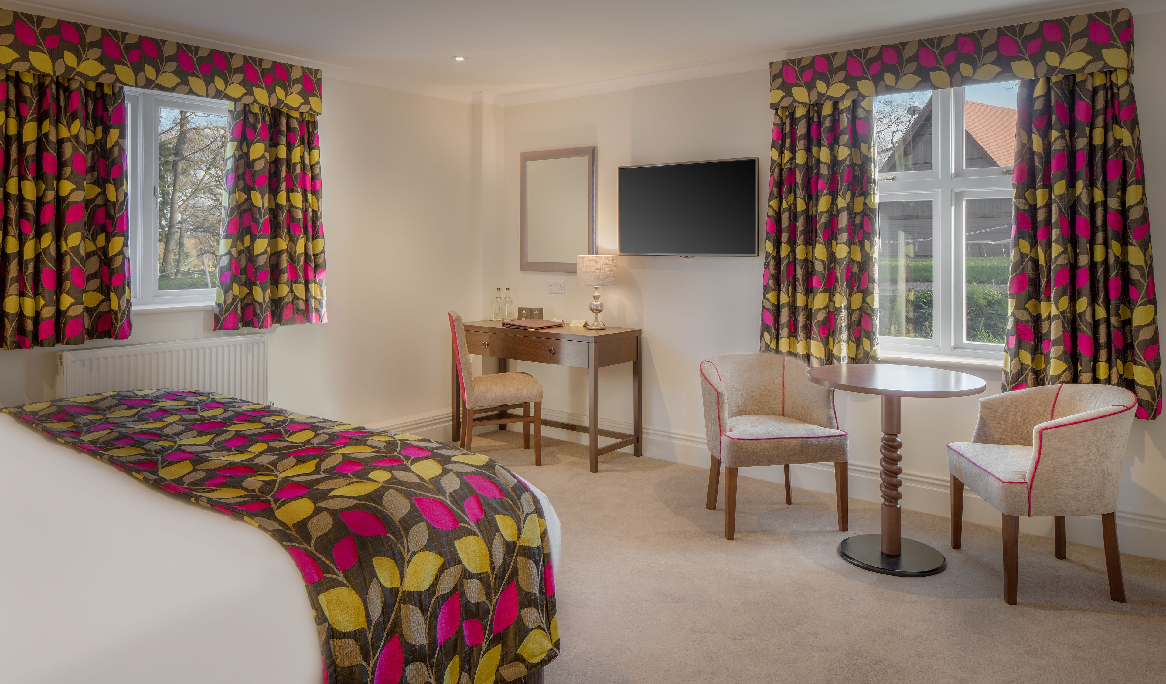 Ein Hotelzimmer mit einem Bett, zwei Stühlen, einem Schreibtisch und einem Fernseher.
