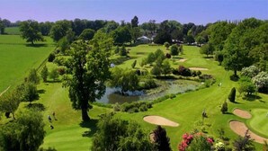 A golf course with a pond, trees, and a clubhouse in the background. - Nailcote Hall Hotel (Solihull)