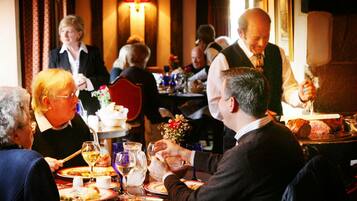 A restaurant with patrons dining at tables, a waiter attending to guests, and a brick wall in the background.