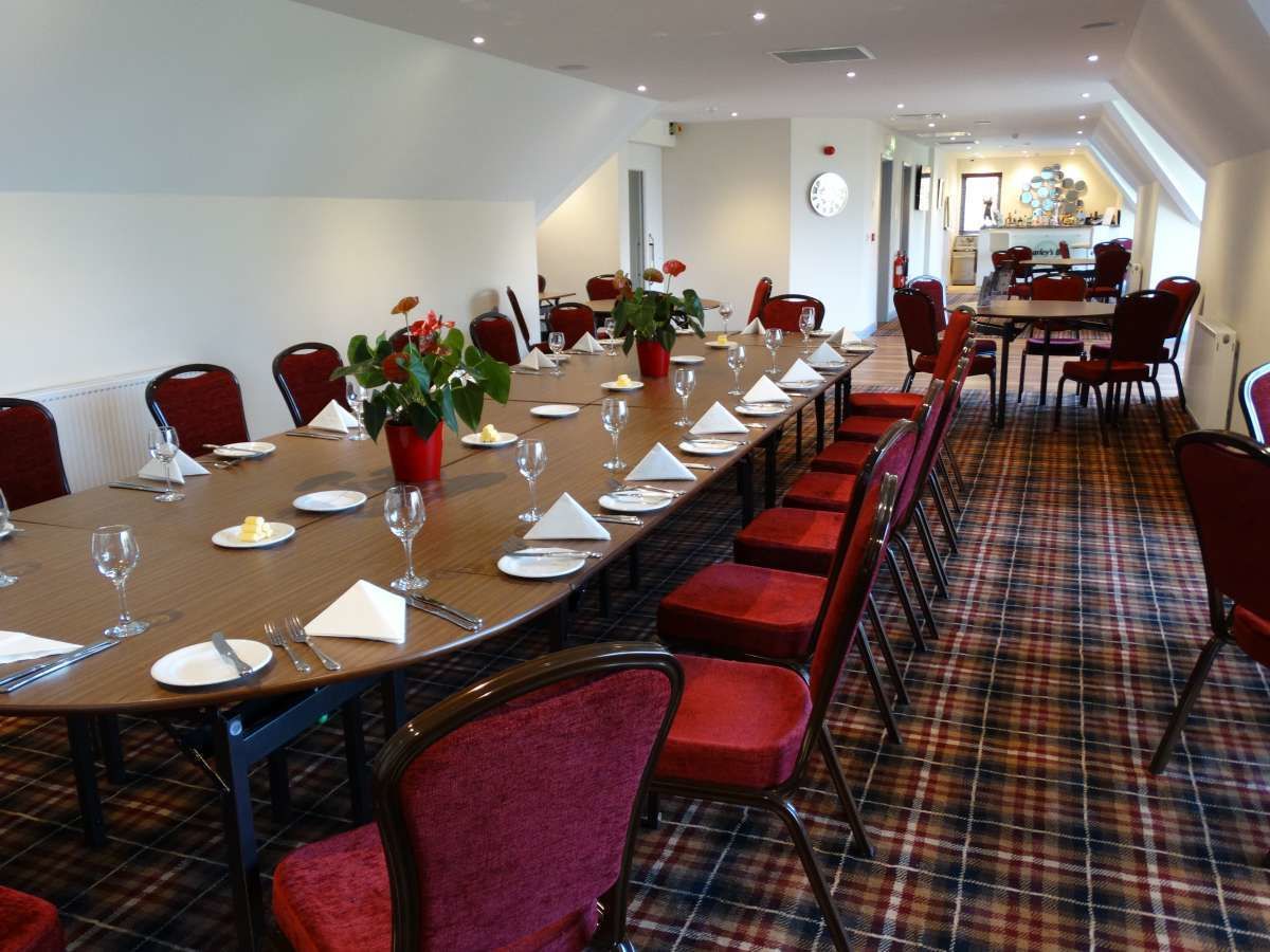 Une salle de conférence avec une longue table préparée pour une réunion, des chaises rouges et un tapis à carreaux.