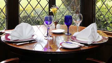 Mesa para dos cubierta, con vista a un jardín a través de una ventana con celosía de diamantes.