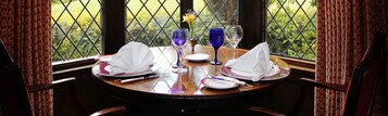 Mesa para dos cubierta, con vista a un jardín a través de una ventana con celosía de diamantes.