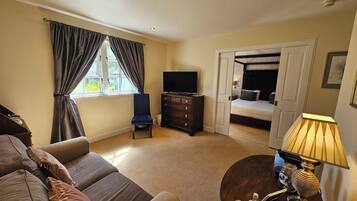A hotel room with a sofa, a television, a dresser, a lamp, and a bed with a headboard.