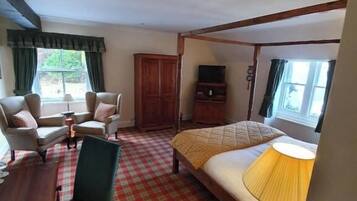 Una habitación de hotel con piso a cuadros, una cama con una lámpara amarilla, dos sillones, un armario de madera y un televisor sobre un soporte.