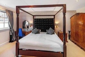 A four-poster bed with a tufted headboard, two pillows, a bedside table with a lamp, and a wooden wardrobe. - Taychreggan, Signature Collection by Eight Continents (Taynuilt)