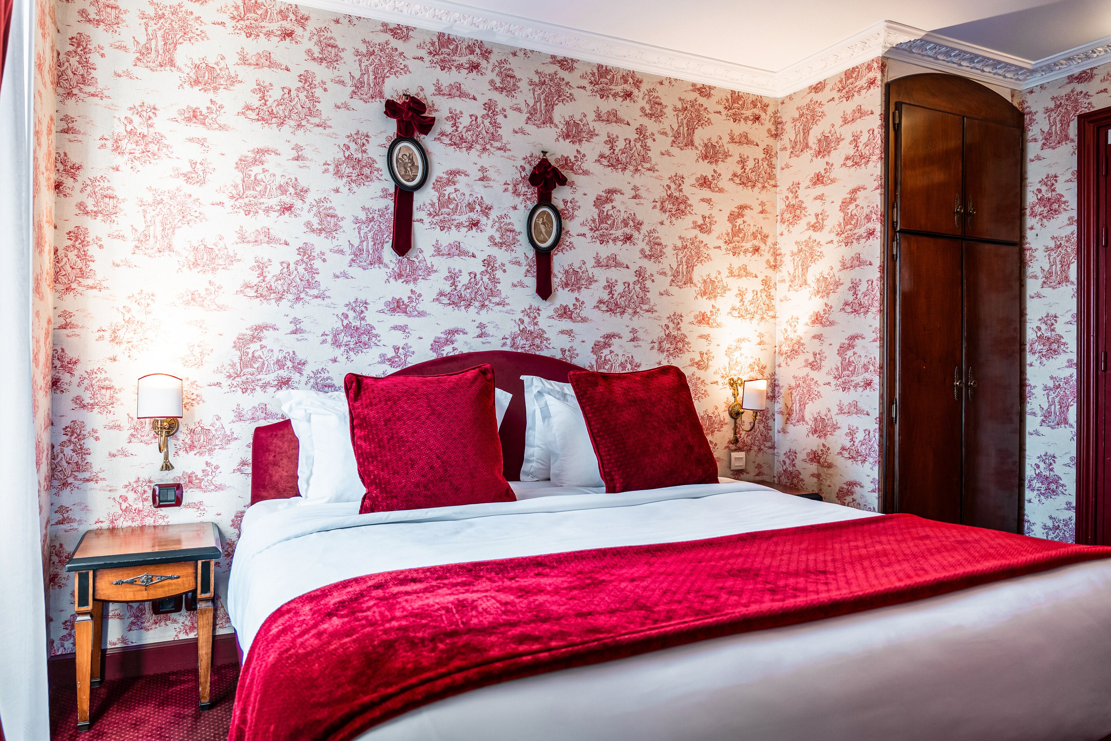 Ein Schlafzimmer mit einem großen Bett, rot-weiß gestreifter Bettwäsche, zwei Wanduhren, einem Nachttisch und einem Holzschrank.