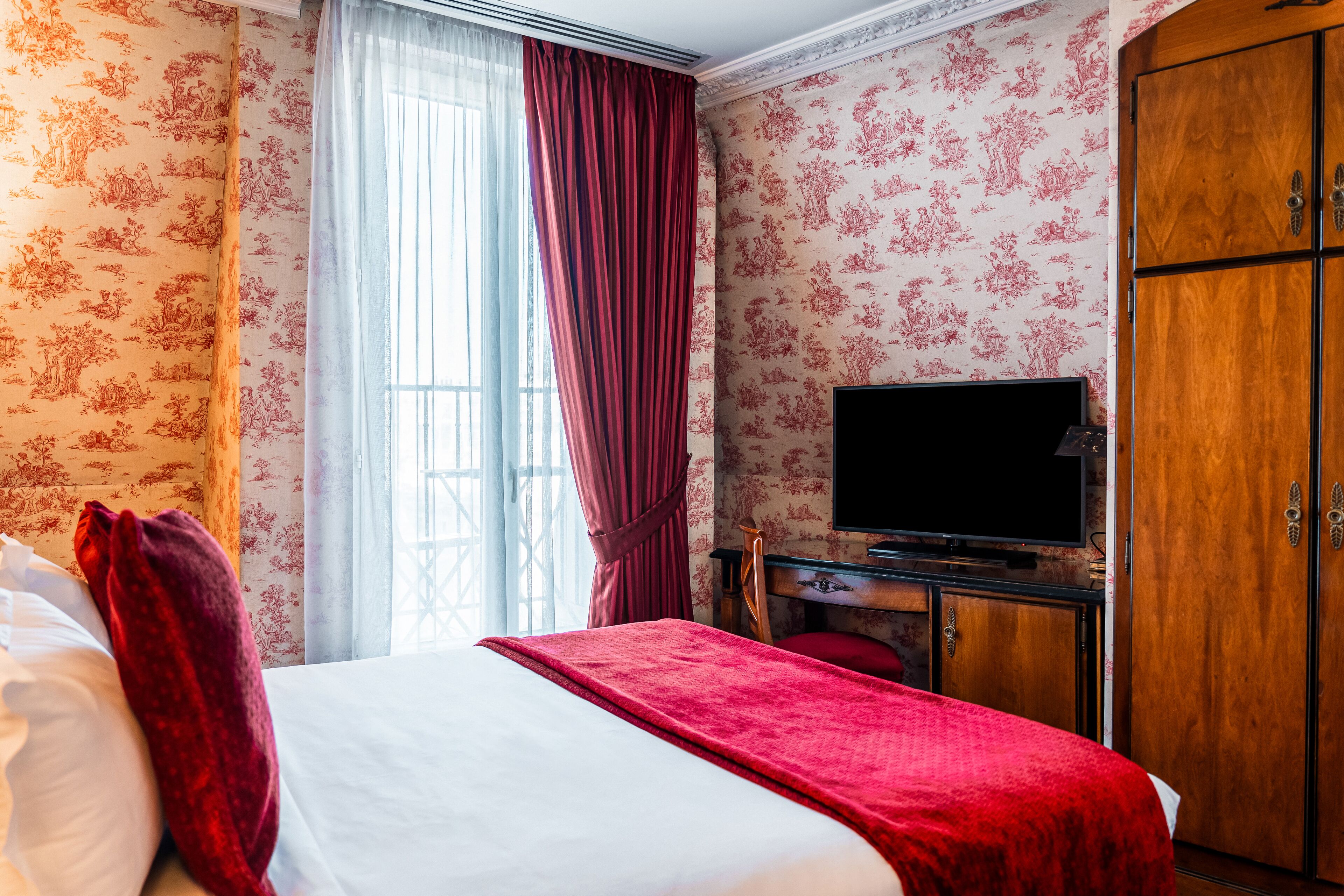 Una camera d'albergo con un letto, una televisione, un armadio in legno e una finestra con tende.