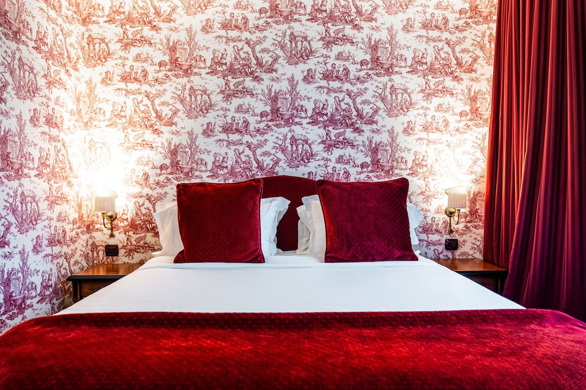 A hotel room with a large bed, red curtains, and a patterned wallpaper.