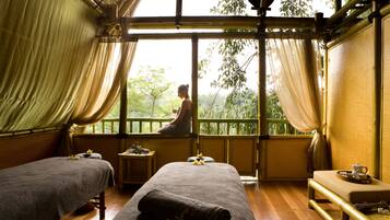 Une chambre avec deux lits, une petite table sur laquelle se trouve une théière, et une vue sur les arbres à travers de grandes fenêtres.