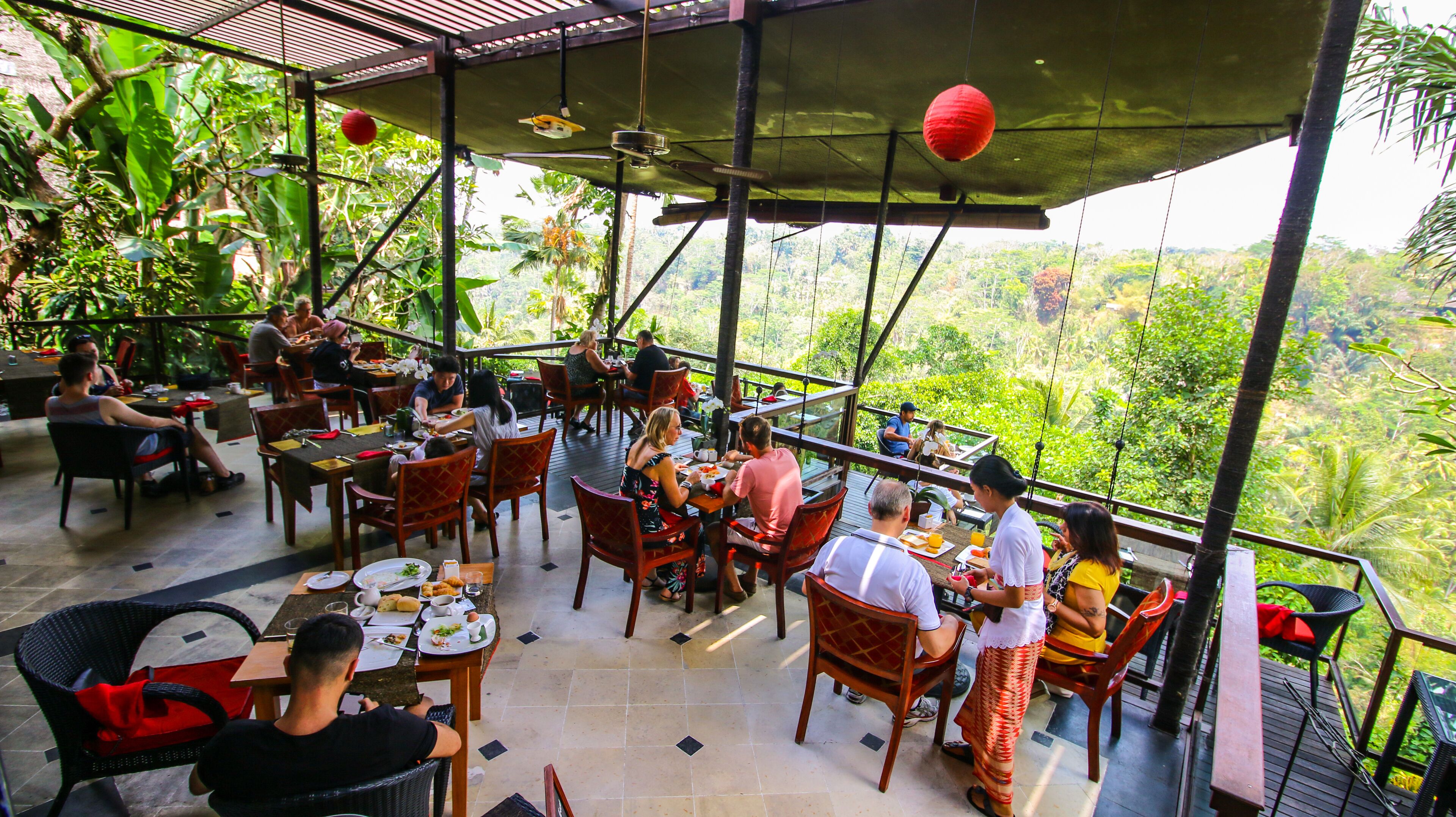 Un restaurante al aire libre con mesas y sillas, rodeado de abundante vegetación y vistas al bosque.