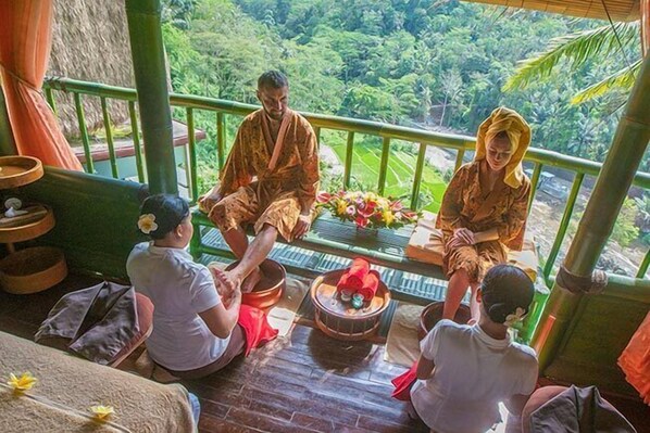 A traditional Balinese ceremony with participants seated on a wooden platform, surrounded by lush greenery.