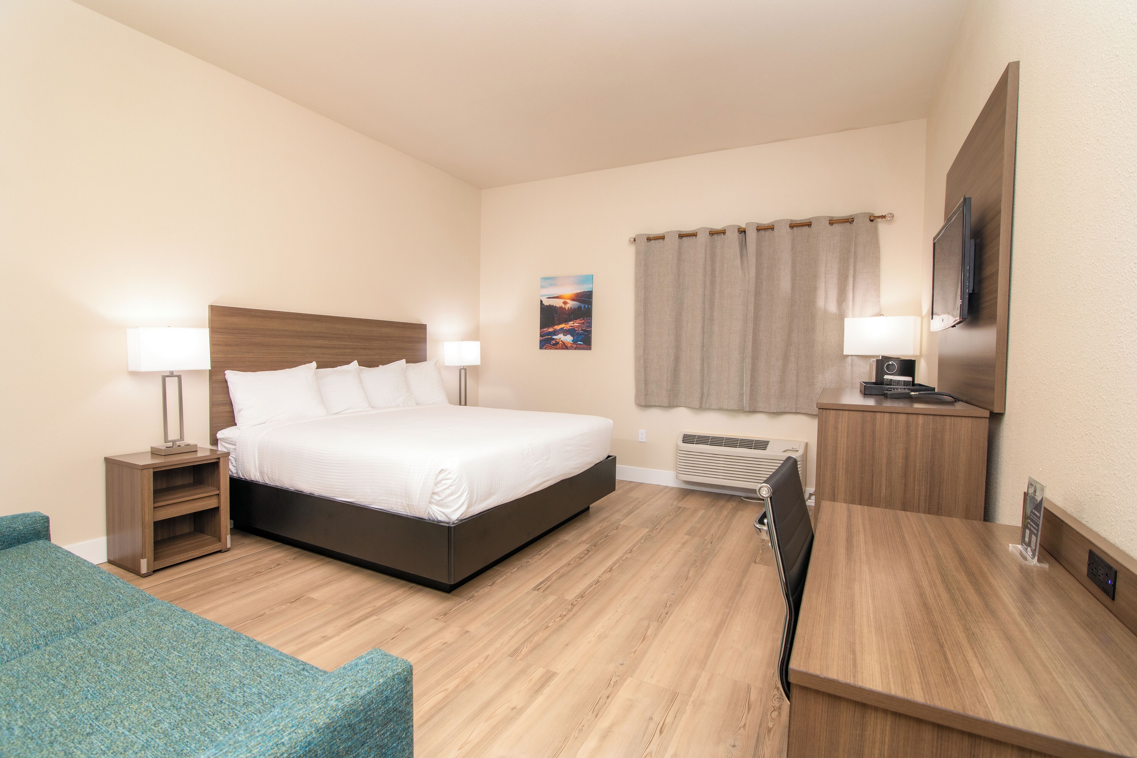 Habitación de hotel con cama, mesitas de noche, escritorio, silla, televisor y ventana con cortinas.