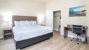 A modern hotel room with a large bed, bedside lamps, a desk with a chair, and a painting on the wall.