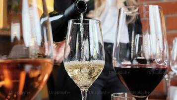 Una persona sirve una bebida en una copa de vino en un bar, con otras copas y una pared de ladrillo al fondo.