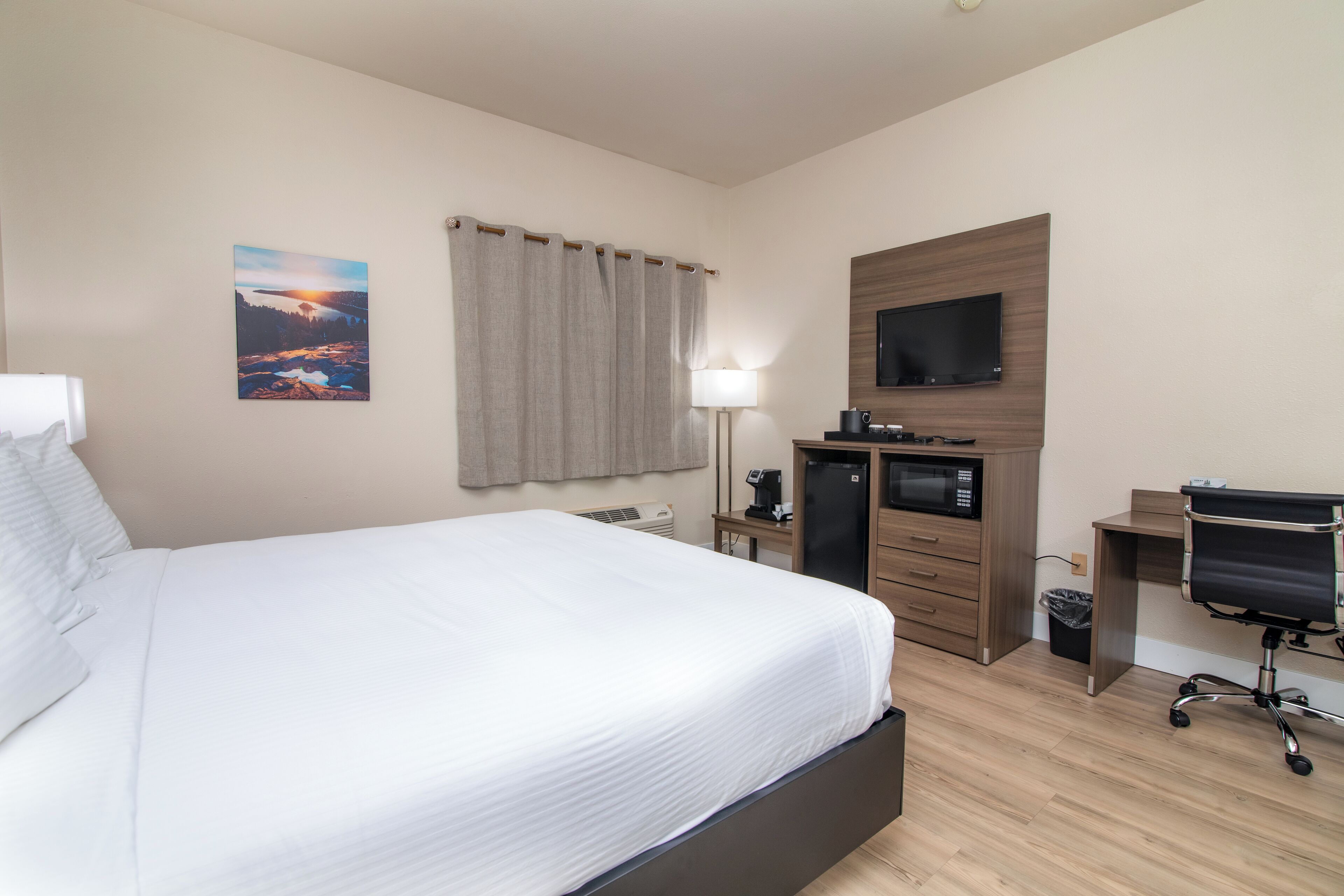 A hotel room with a bed, a desk with a computer, a TV, a lamp, and a picture on the wall.