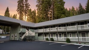 A motel with a two-story structure, a covered parking area, and a forested backdrop.