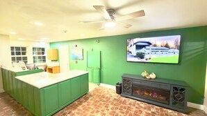 Une cuisine avec des meubles de couleur verte, un plan de travail blanc, une cheminée et un téléviseur fixé au mur.