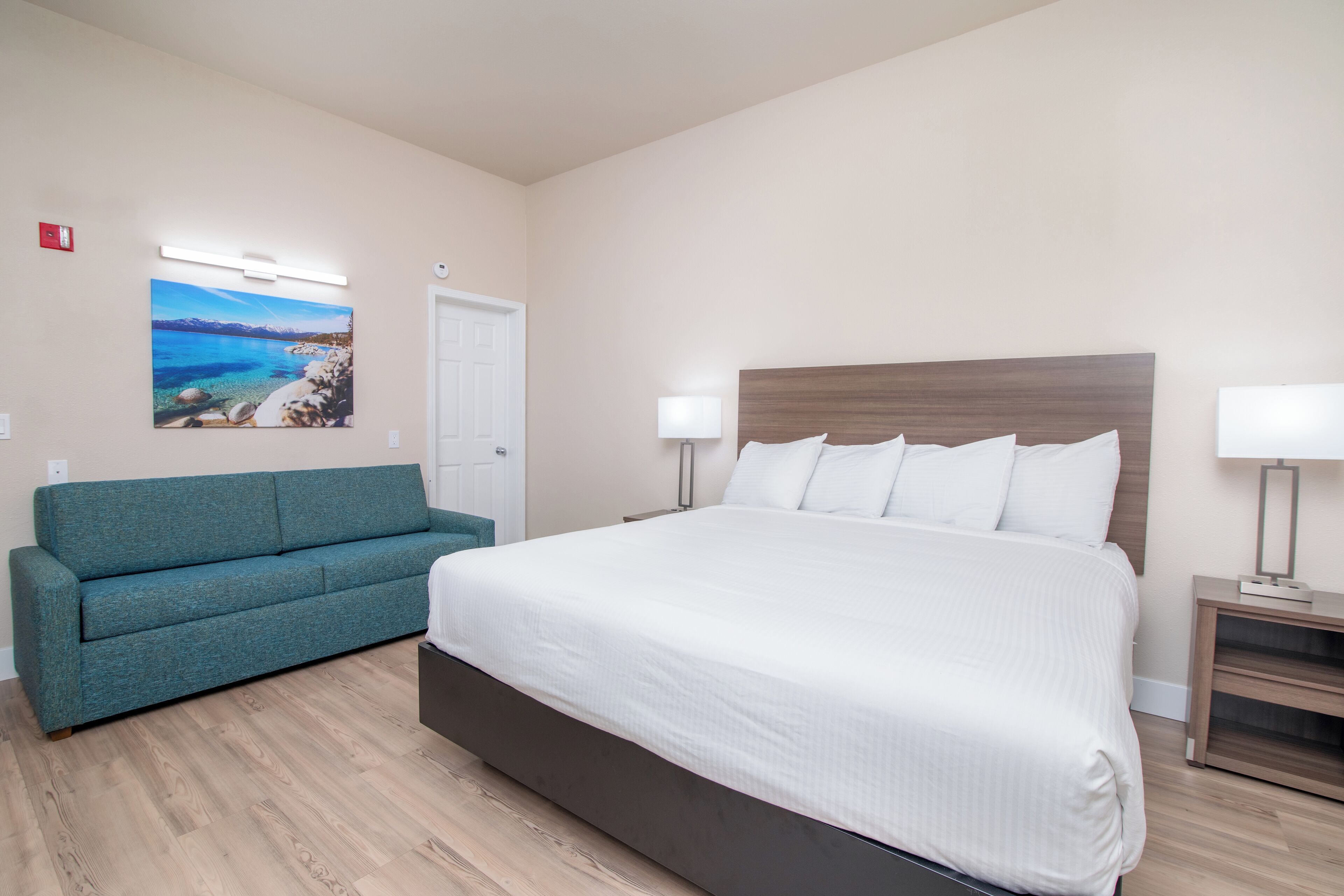 Un dormitorio con una cama grande, un sofá color turquesa y un cuadro de una escena costera.