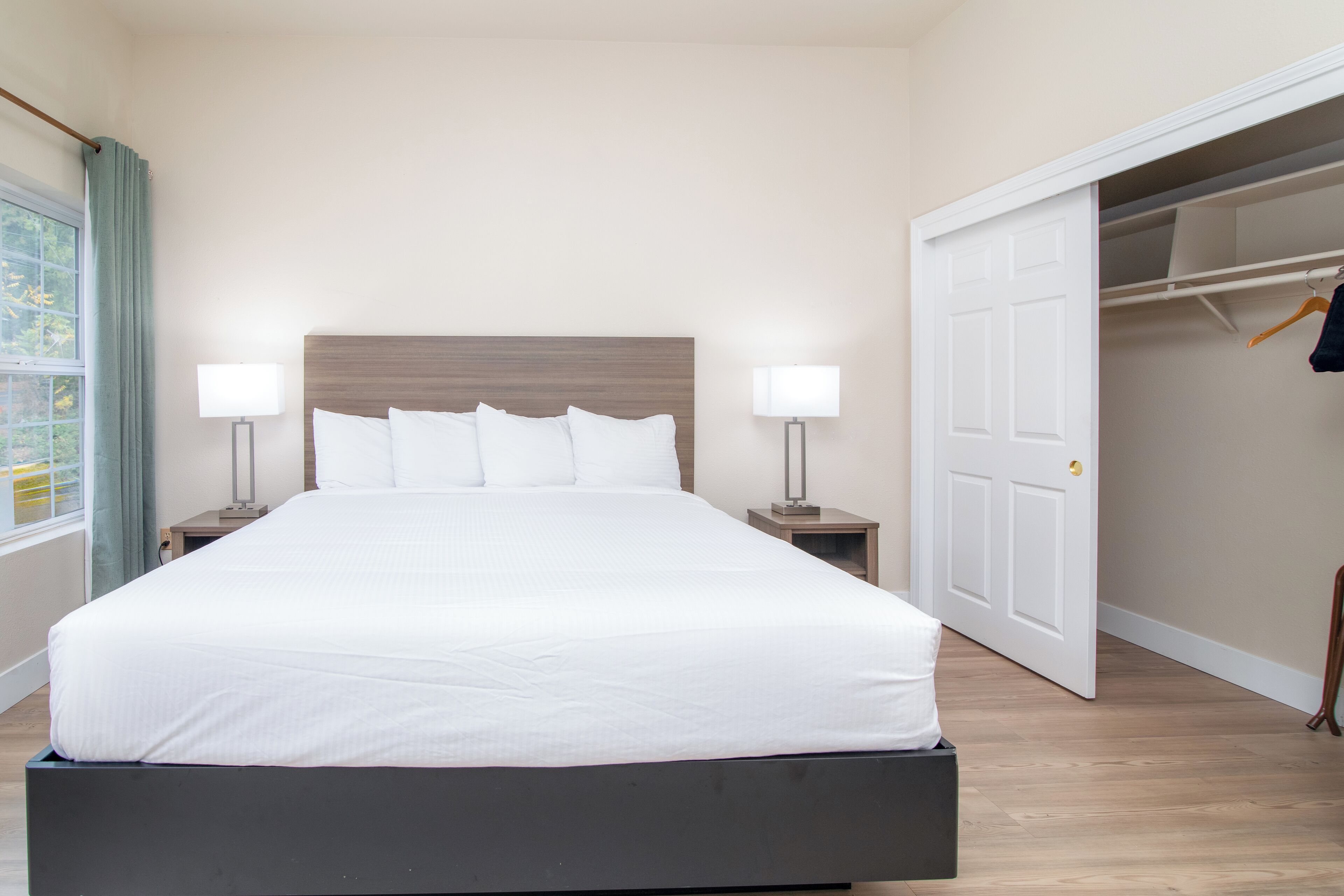 A neatly made bed with white linens in a room with a wooden floor and a white door.