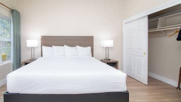 A neatly made bed with white linens in a room with a wooden floor and a white door.
