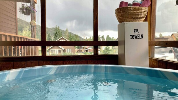 A hot tub with a view of a mountain landscape, a basket of towels, and a sign reading 'SPA TOWELS.' - Big Horn Lodge (Grand Lake)