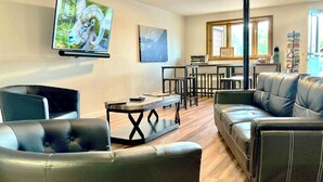 A living room with a black leather sofa, a black armchair, a coffee table, and a TV mounted on the wall. - Big Horn Lodge (Grand Lake)