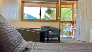 A room with a bed, a chair, a small table, a window, and a door leading outside. - Big Horn Lodge (Grand Lake)