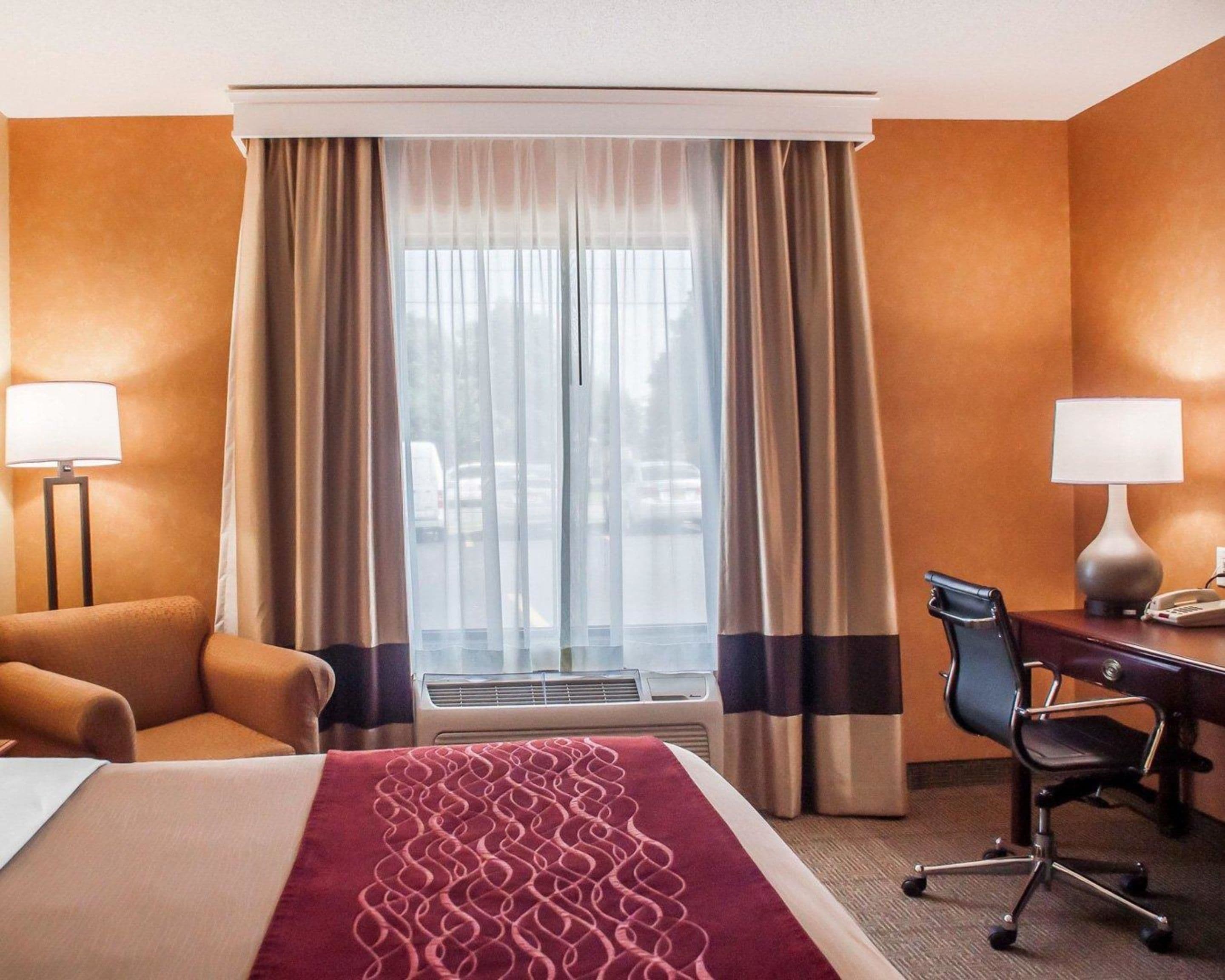 Habitación de hotel con cama, escritorio, silla, dos lámparas y ventana con cortinas.