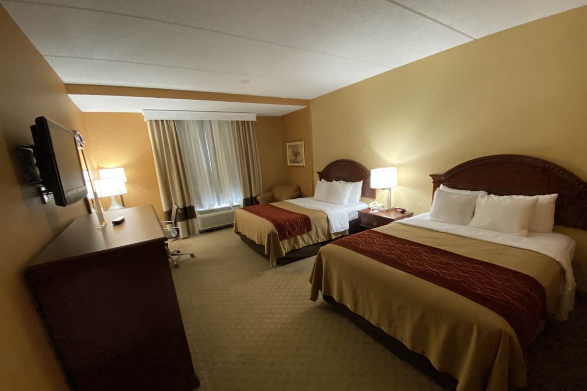 A hotel room with two beds, a desk, a chair, a TV, and a window with curtains.